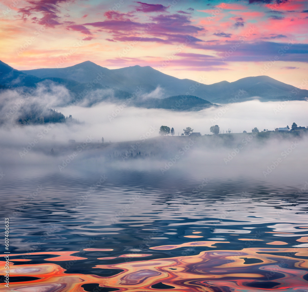 Carpathian mountains reflected in the calm waters of small pond. Misty autumn scene of mountain valley. Picturesque morning scene of Ukrainian countryside. Landscape photography.