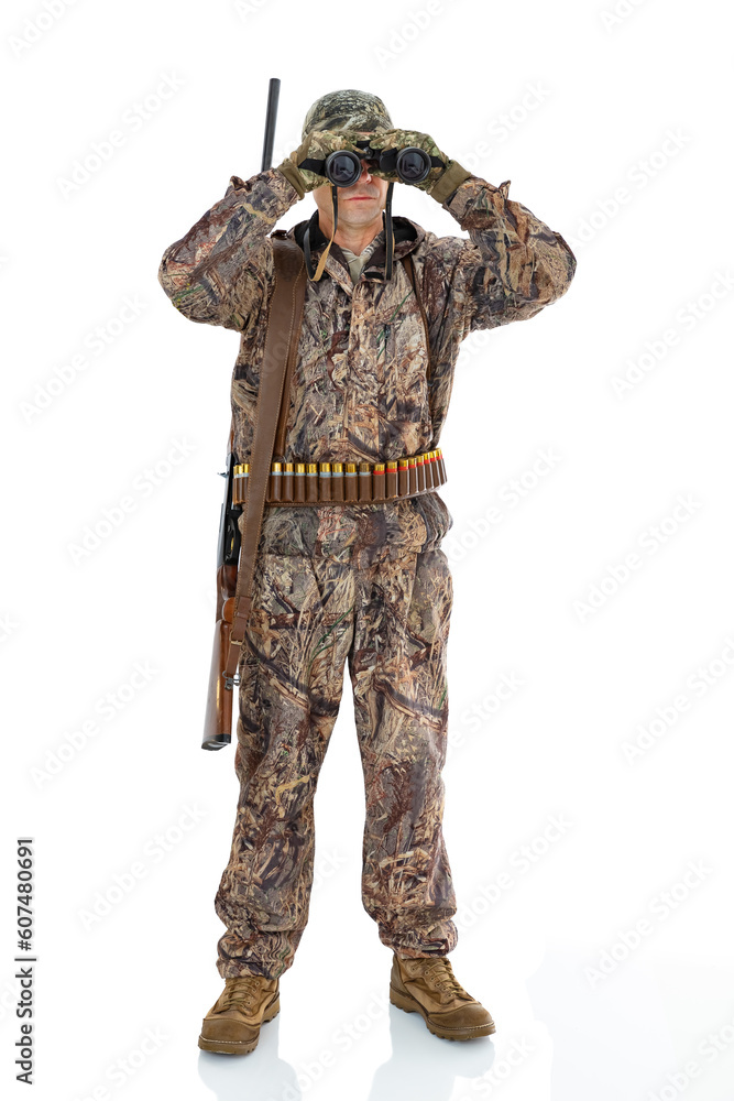 Full length portrait of a mature hunter with a shotgun looks through binoculars to the side, isolated on white background. Duck hunter with a rifle on his shoulder posing in studio. Full length portrait of a mature hunter with a shotgun looks through binoculars to the side, isolated on white background. Duck hunter with a rifle on his shoulder posing in studio.