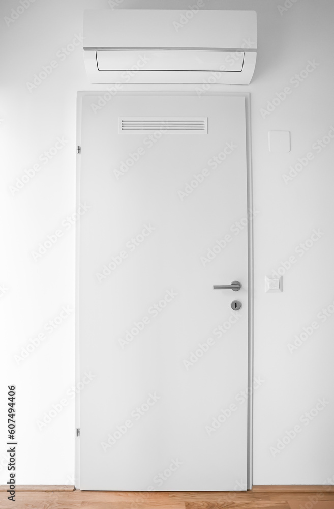 White door and modern air conditioner hanging on light wall White door and modern air conditioner hanging on light wall