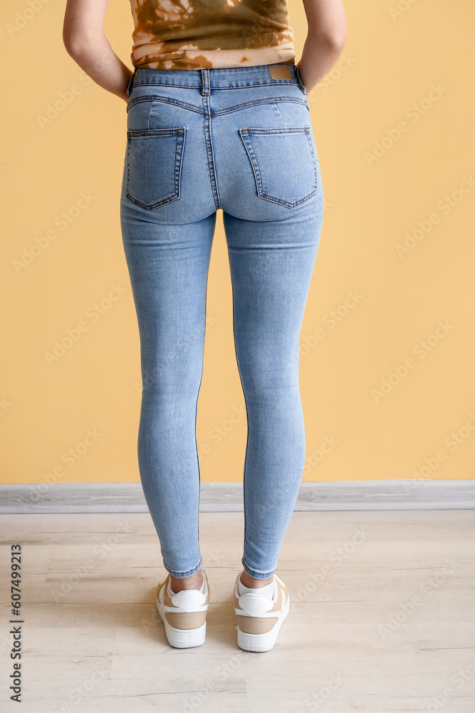 Young woman in stylish jeans near yellow wall, back view Young woman in stylish jeans near yellow wall, back view