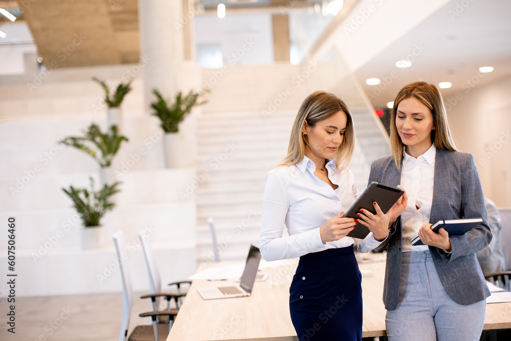 Fototapeta premium Two young business women looking at financial results on digital tablet in front of their team at the office