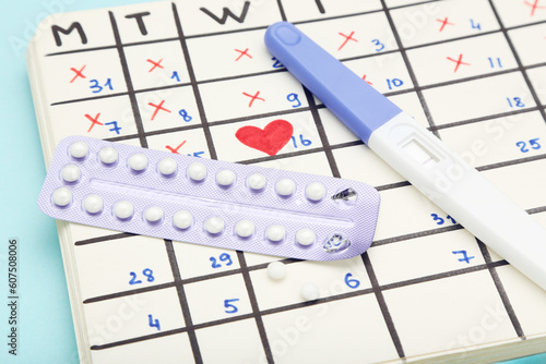 Oral contraceptive pills with pregnancy test and calendar on blue background