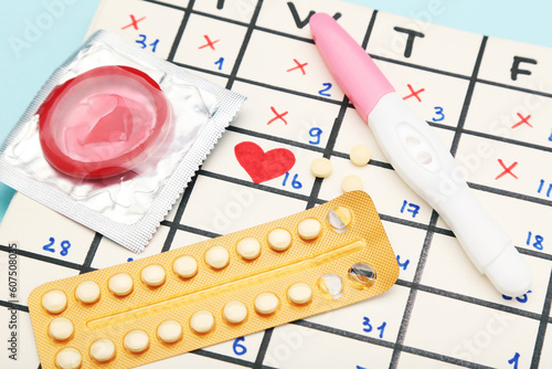 Oral contraceptive pills with condom, pregnancy test and calendar on blue background