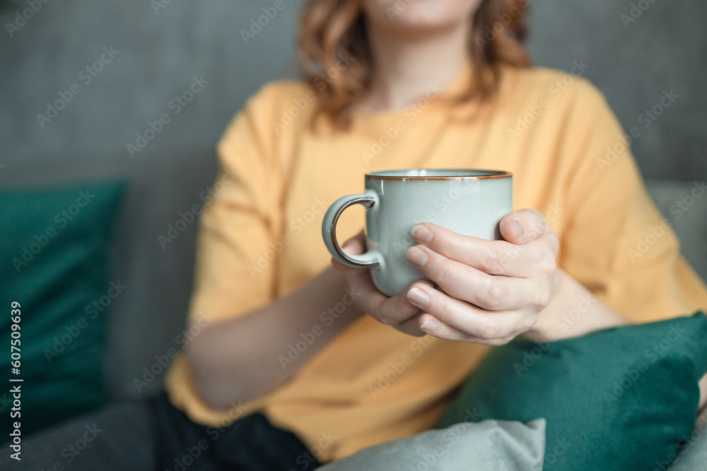 Close up of a beautiful happy girl sitting on couch drinking hot coffee and enjoying morning, being in dreamy and relaxed mood. 