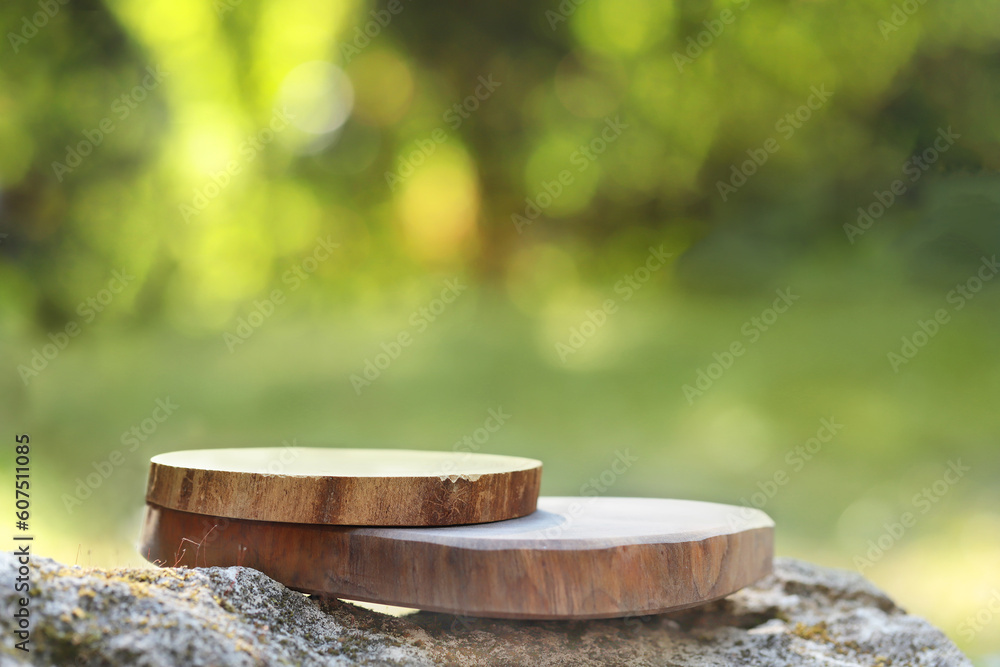 A podium made of sawn wood with a natural background on the stones. Front showcase with a stand for the presentation of goods. With a beautiful view of juicy greenery with bokeh.