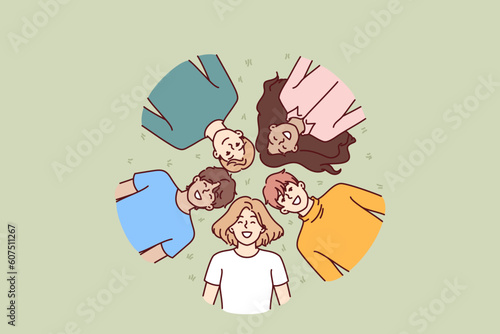 Happy children lie on green grass and smile while enjoying walk in park in hot summer weather. Top view of faces of multiethnic children boys and girls lying in clearing on sunny day