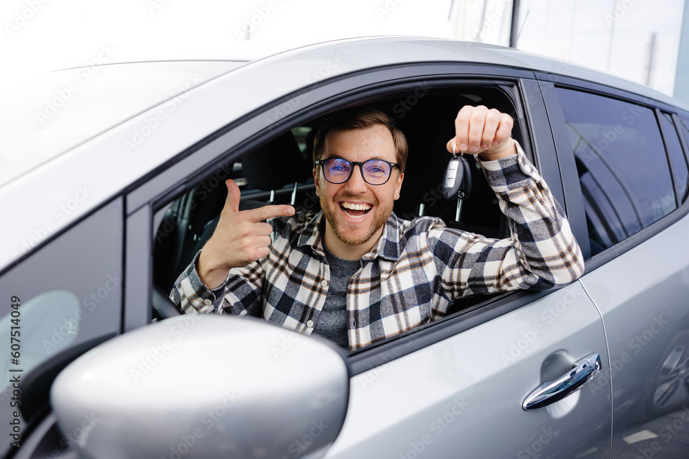 Excited young man showing a car key, sitting inside his new vehicle Excited young man showing a car key, sitting inside his new vehicle