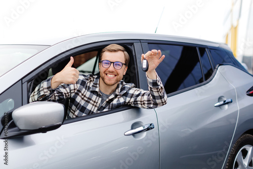 Excited young man showing a car key, sitting inside his new vehicle © nazariykarkhut