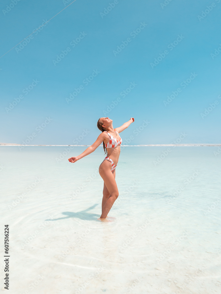 Beautigul girl in swimming suit on Dead sea salt crystals formation coastline, clear cyan green water at Ein Bokek beach, Israel