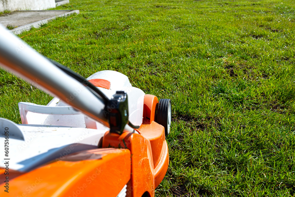 A small motorized electric mower standing on the lawn, it is orange in color.