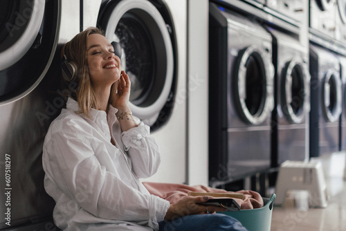 Obraz na plátně Young woman listening music, waiting in a laundry room.