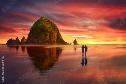 Beautiful view at sunset of Cannon Beach with Haystack Rock. A couple (two people) enjoying a colorful summer sunset over Haystack Rock in Cannon Beach (Oregon coast), USA