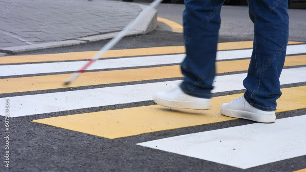 Close-up of the legs of a blind woman crossing the road at a crosswalk with a cane. 