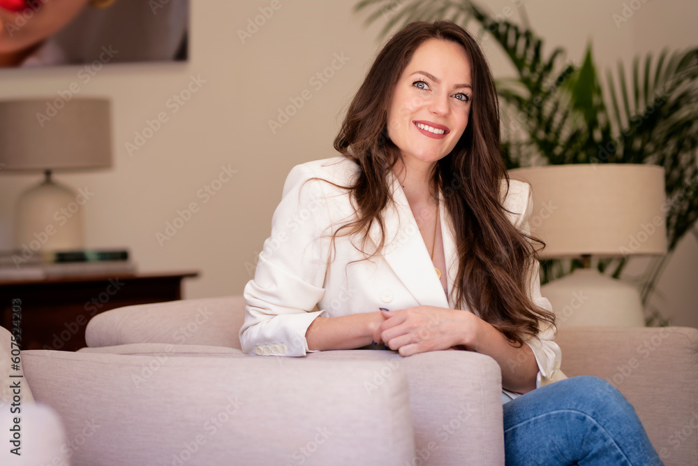 Portrait of brunette haired young woman wearing white blazer and relaxing in an armchair at home Portrait of brunette haired young woman wearing white blazer and relaxing in an armchair at home