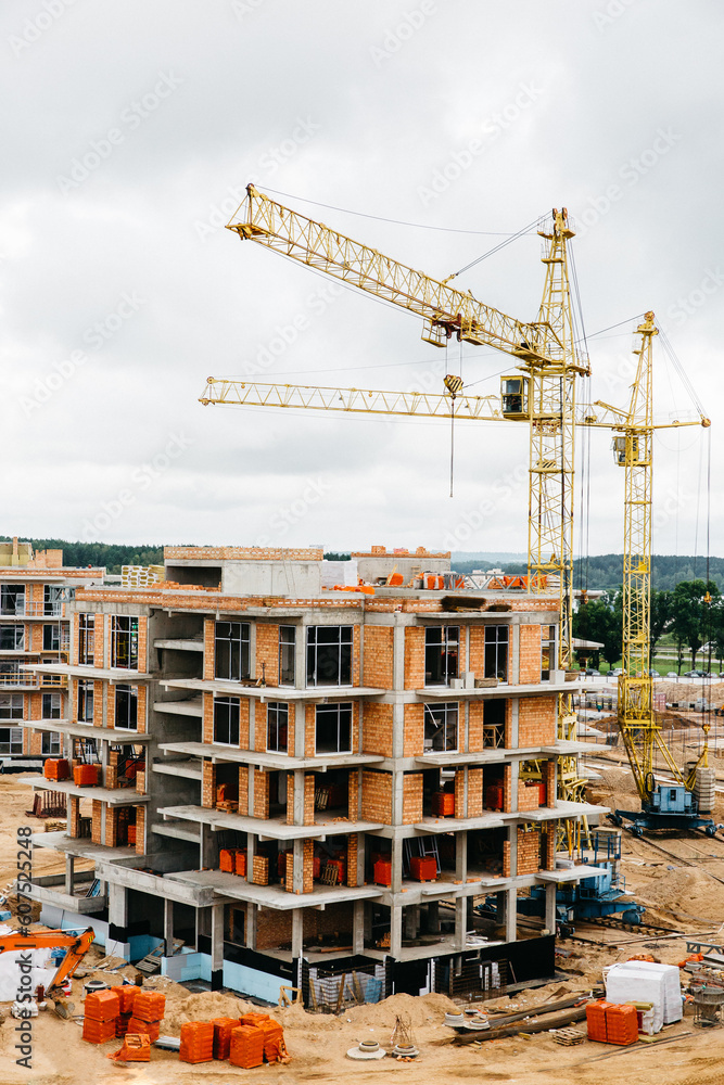 vertical photo of two cranes near building. Concrete building under construction