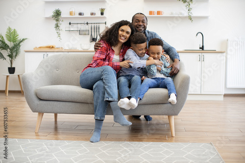 Fotografija Full length portrait of multiethnic kids with female resting on couch while happy man embracing everyone in kitchen