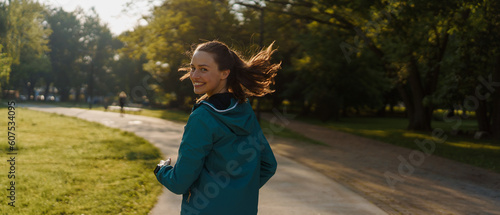 Fototapeta Naklejka Na Ścianę i Meble -  Portrait of smilling young woman running in the city park in the early morning.