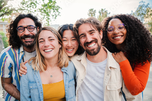 Portrait of a group of friends laughing together and looking at camera. Five young multiracial cherful people smiling and having fun. Joyful startup team coworkers celebrating and bonding together