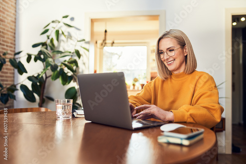Happy mature woman using laptop while working remotely from home in living room photo
