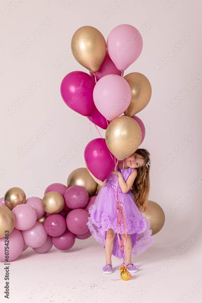 Cute happy little girl in a lilac princess dress posing with air balloons isolated on white background. Kids Birthday party celebration concept. Happy Birthday banner with copy space. Studio shot. Cute happy little girl in a lilac princess dress posing with air balloons isolated on white background. Kids Birthday party celebration concept. Happy Birthday banner with copy space. Studio shot.
