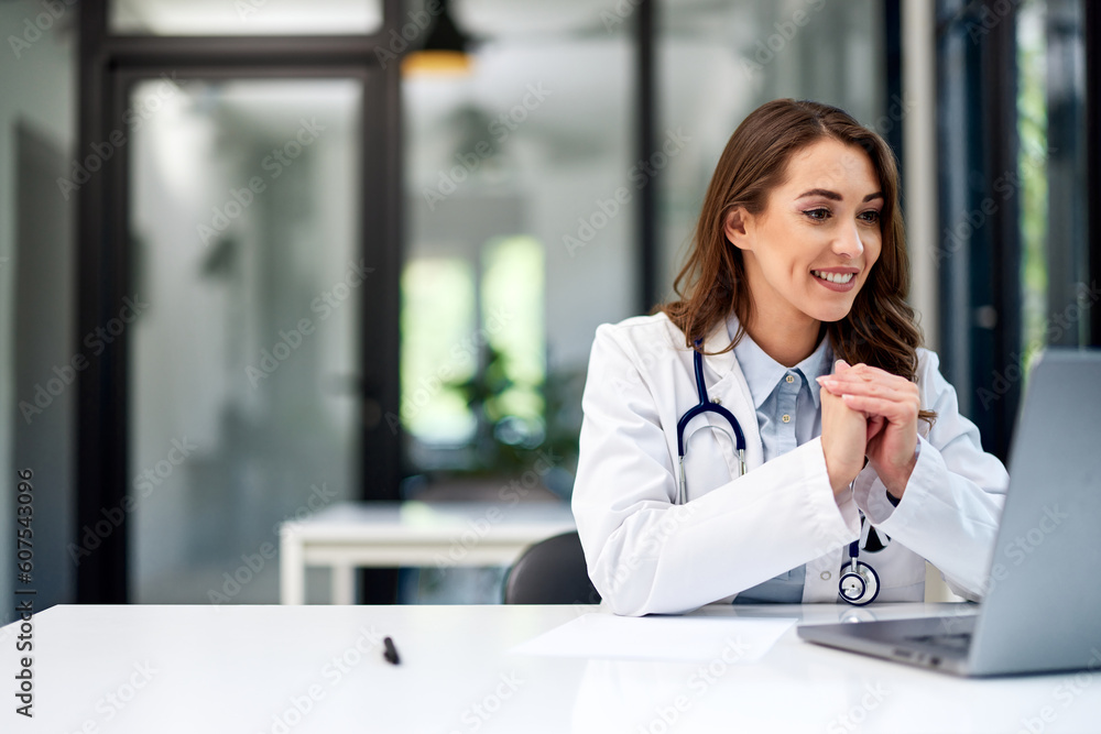 © bnenin - A smiling female doctor having an online video call over a laptop at the office. © bnenin - A smiling female doctor having an online video call over a laptop at the office.