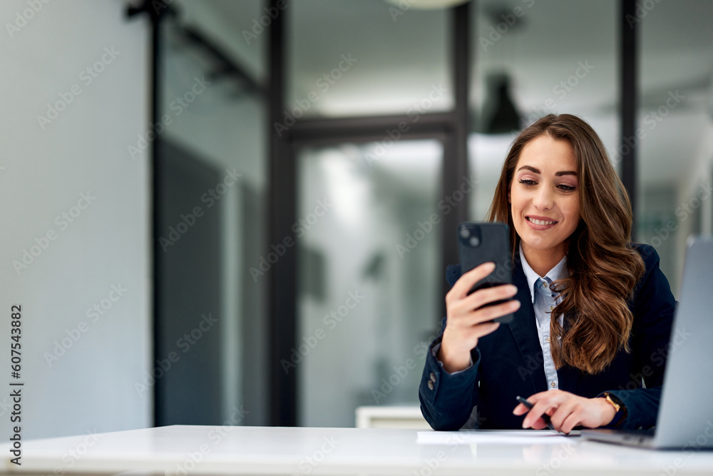 A smiling businesswoman using a mobile phone while working at the office. A smiling businesswoman using a mobile phone while working at the office.