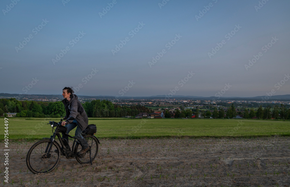 Obraz premium Electric bike with black bag on meadow and field near Budweis in evening