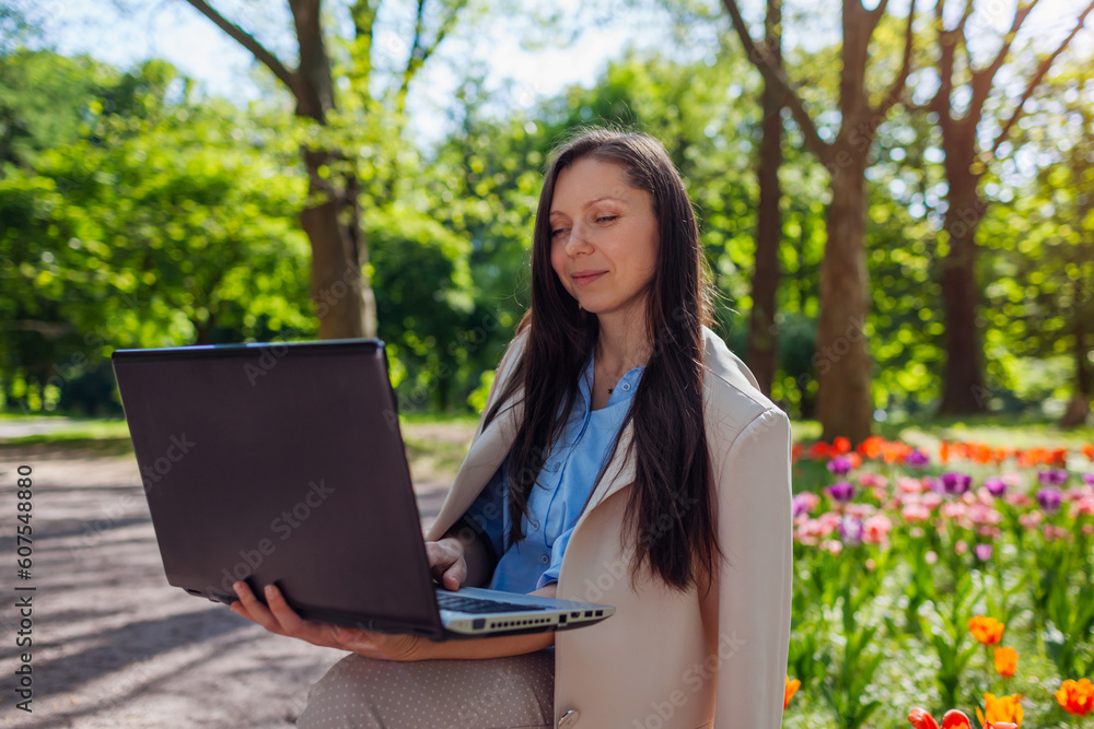 Outdoor portrait of young businesswoman working in spring park on laptop. Female landscape designer enjoys results Outdoor portrait of young businesswoman working in spring park on laptop. Female landscape designer enjoys results