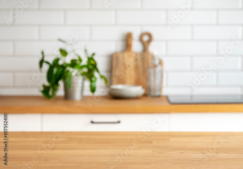 Wooden tabletop with free space for product montage or mockup against blurred white kitchen with cutting board and plant in scandinavian style