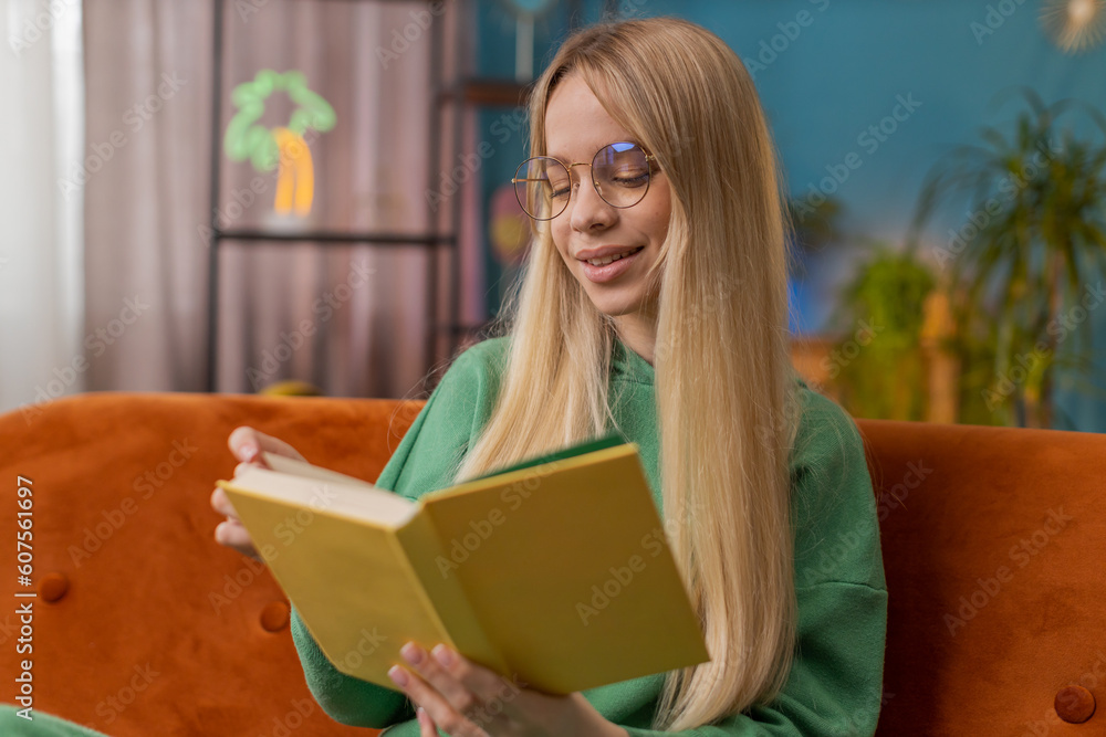 Young Caucasian woman relaxing interesting book turning pages smiling enjoying literature, taking a rest on comfortable couch. Portrait of peaceful cheerful girl at home apartment living room on couch Young Caucasian woman relaxing interesting book turning pages smiling enjoying literature, taking a rest on comfortable couch. Portrait of peaceful cheerful girl at home apartment living room on couch