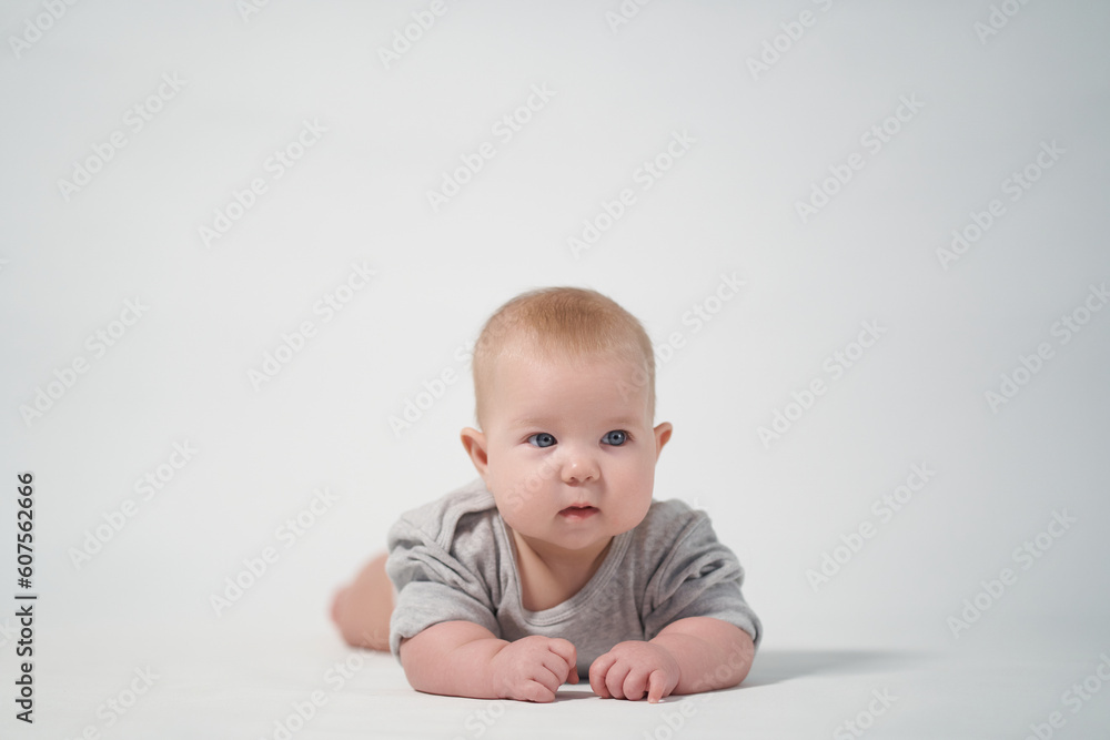 Portrait of a baby on a light background in gray clothes. The baby lies on his stomach. studio photography Portrait of a baby on a light background in gray clothes. The baby lies on his stomach. studio photography