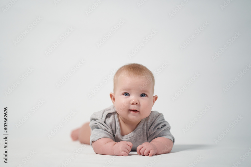 Portrait of a baby on a light background in gray clothes. The baby lies on his stomach. studio photography Portrait of a baby on a light background in gray clothes. The baby lies on his stomach. studio photography