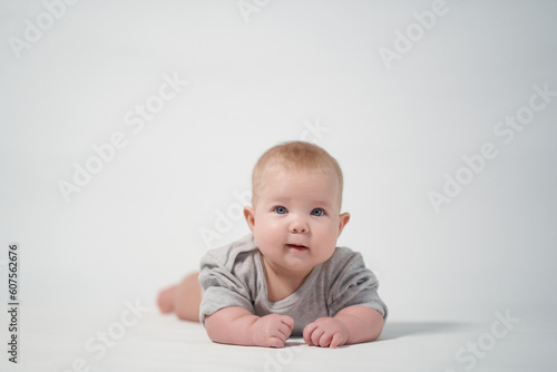 Portrait of a baby on a light background in gray clothes. The baby lies on his stomach. studio photography