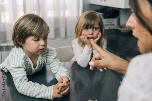 Mother scolding and pointing fingers at her pair of blonde children in the kitchen.