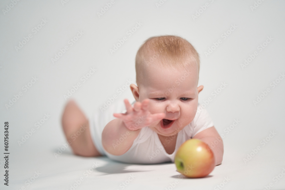 A 7 month old child reaches out to an apple. photography on a white background A 7 month old child reaches out to an apple. photography on a white background