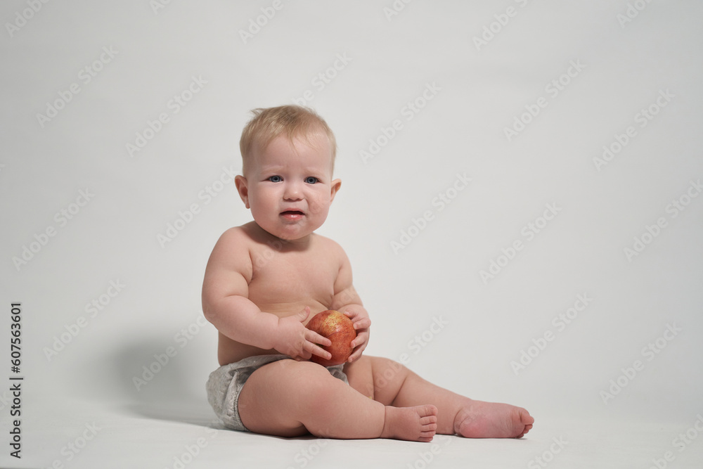 a child of 7 months sitting on the pope holds a red apple in his hands. photography on a light background a child of 7 months sitting on the pope holds a red apple in his hands. photography on a light background