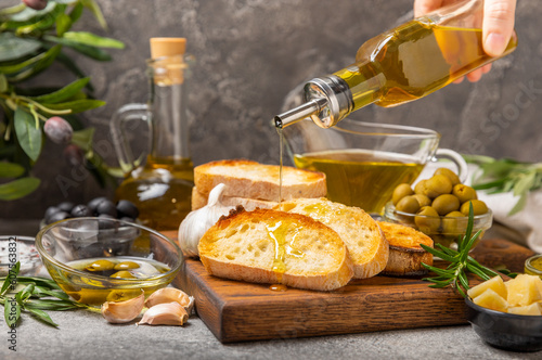 Fotografie Ciabattas, olive oil in a bowl with olives, herbs, spices, garlic, pesto, parmesan and ciabatta bread on a texture background