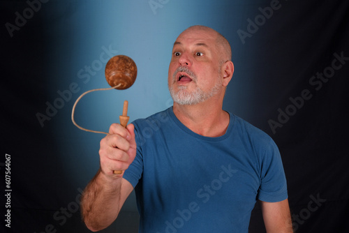 happy bald man with white beard playing with antique children's toy bilboquet looking forward with good expression