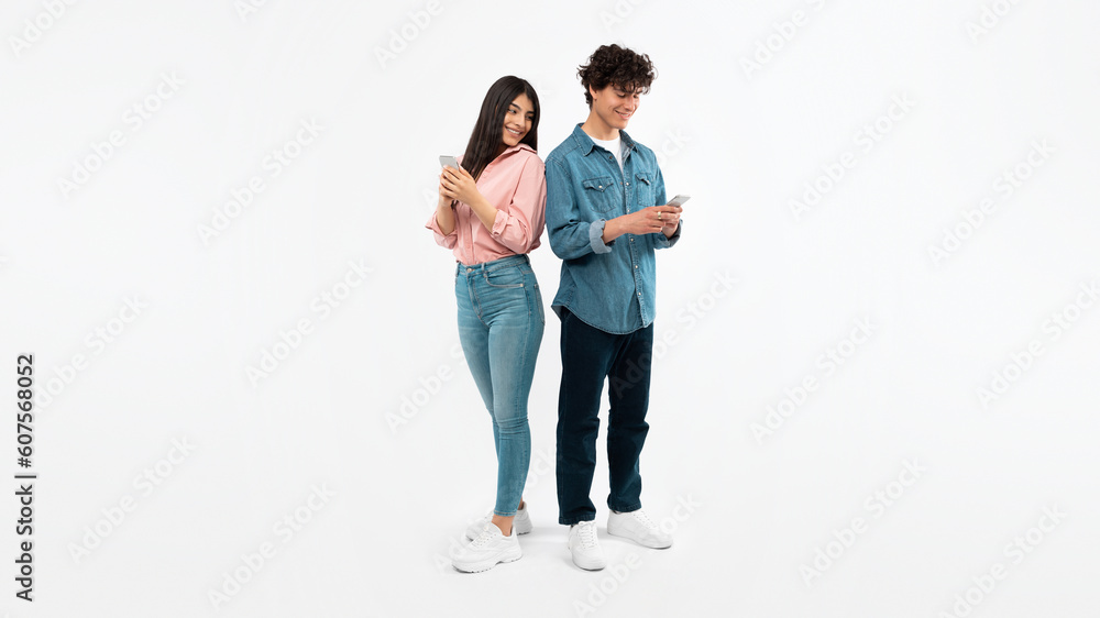 Young Couple Using Mobile Phones Texting Standing On White Background Young Couple Using Mobile Phones Texting Standing On White Background