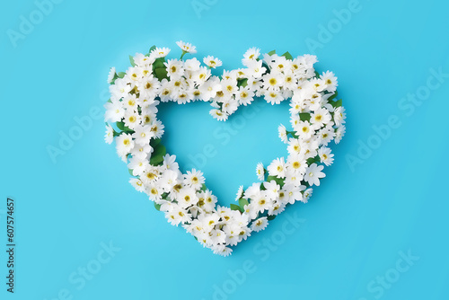 White daisies wreath in the shape of a heart on blue background. Festive background with copy space. Natural floral wallpaper for mother's, father's day, birthday. 