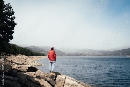 hombre con chaqueta roja de espaldas mirando el paisaje de un lago de montaña