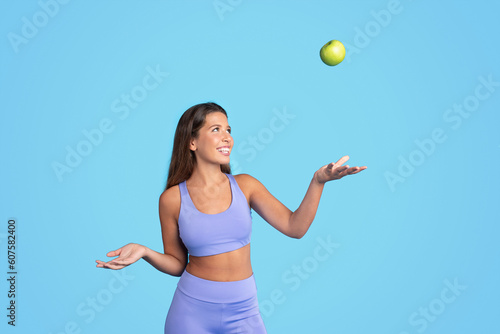 Smiling young european slim woman athlete brunette in sportswear tossing green apple, has fun © Prostock-studio