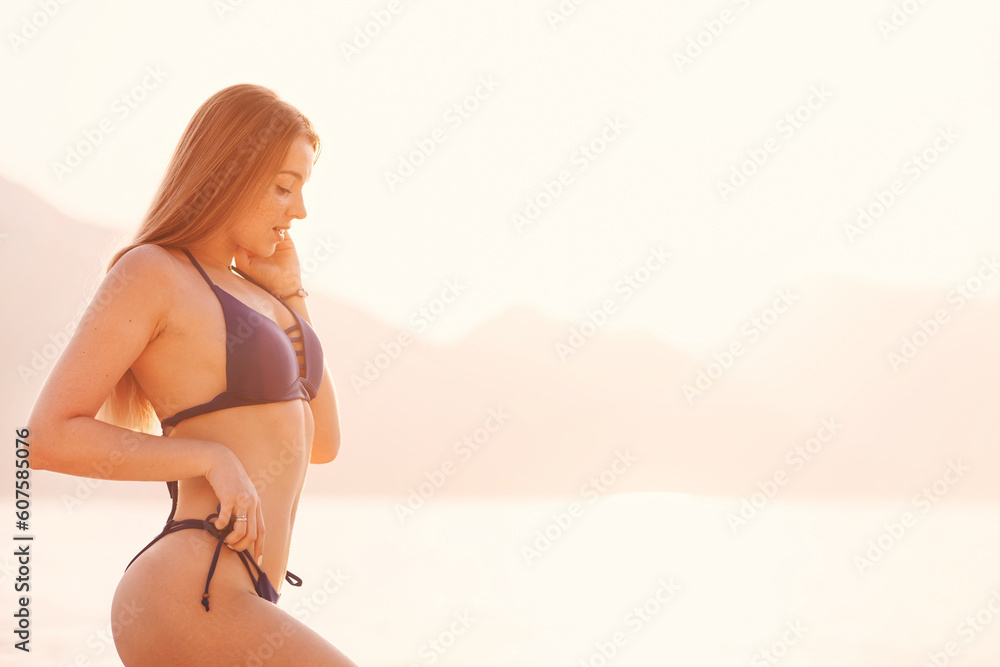 Fototapeta premium Attractive woman with perfect body wearing swimsuit and on the beach in sunset. The concept of sea recreation. Copy space