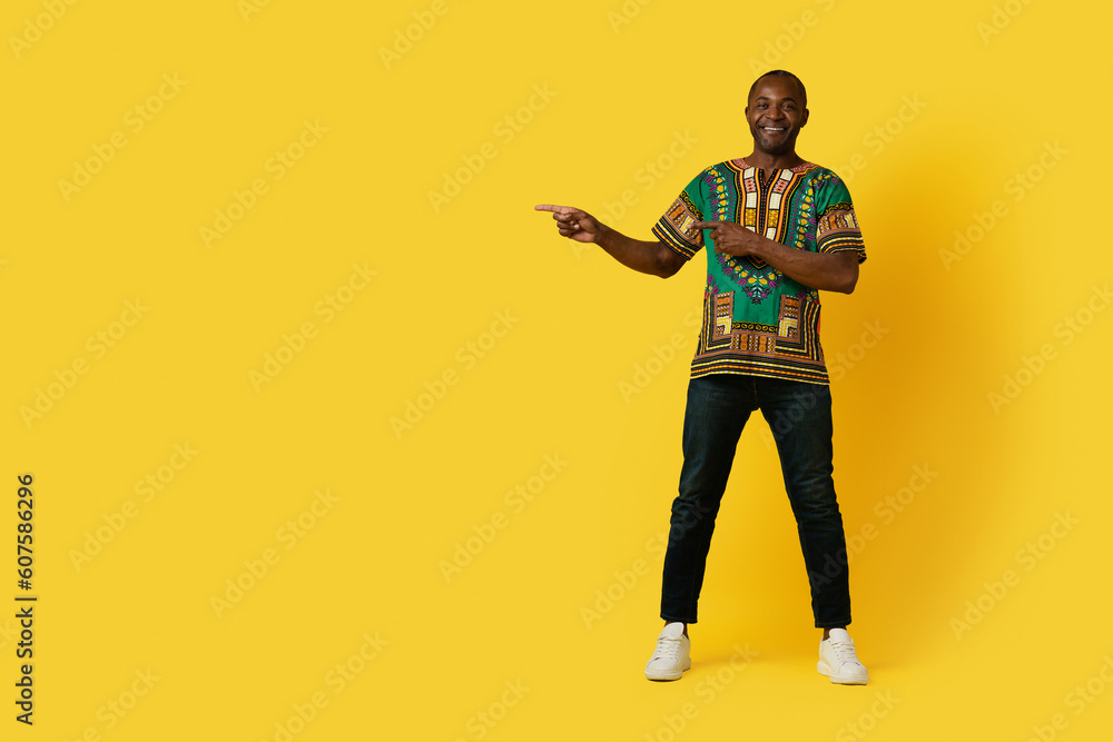Fototapeta premium Cheerful black man in traditional shirt pointing at copy space