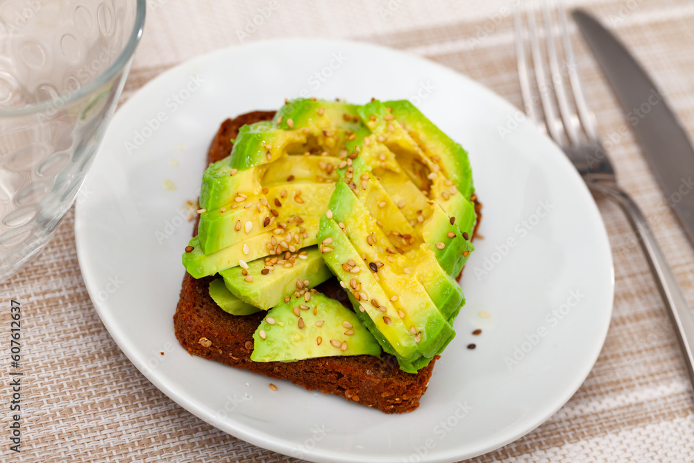 Sandwich with pieces of fresh avocado and sesame served on plate.