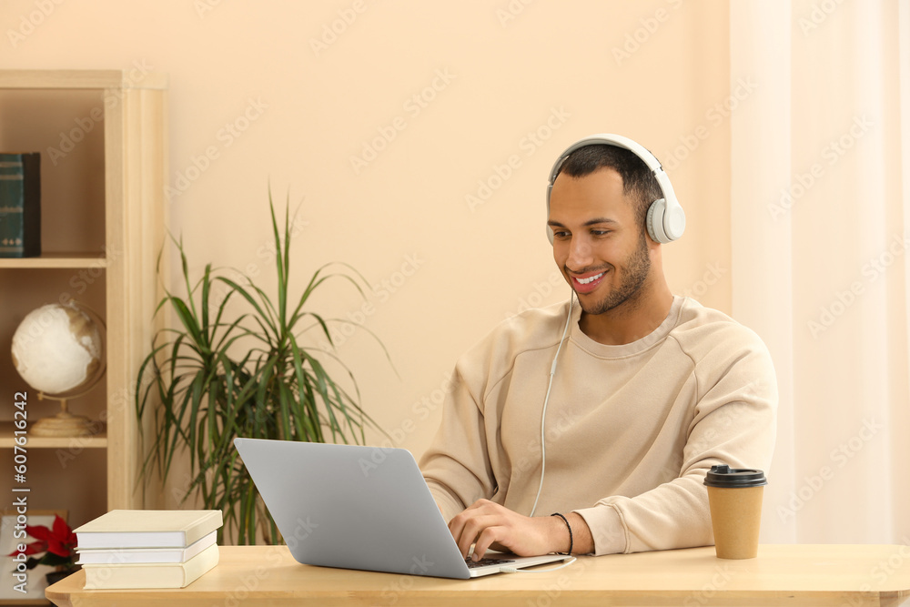 Smiling African American man in headphones working on laptop at wooden table indoors Smiling African American man in headphones working on laptop at wooden table indoors