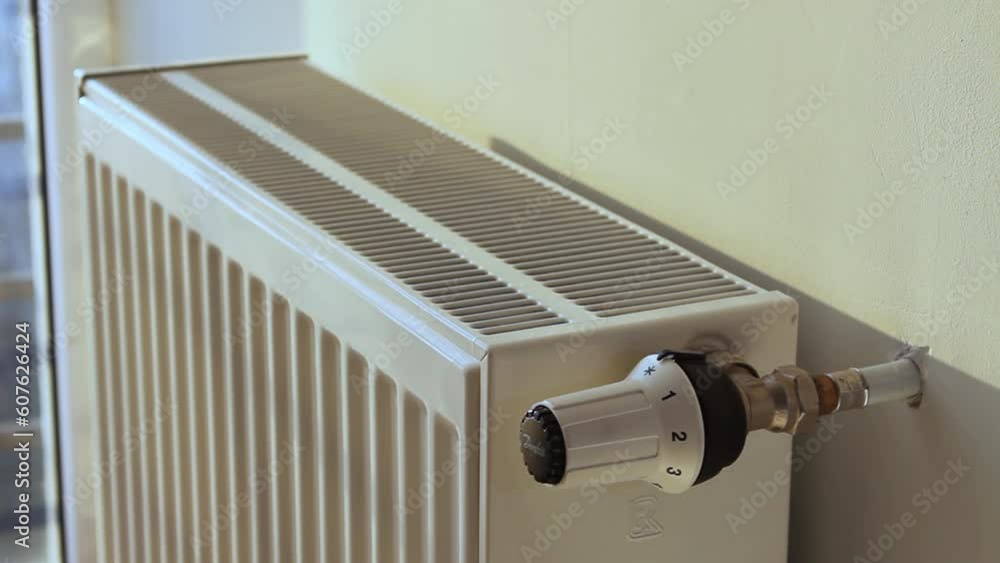 The man turns off the heating by setting the thermostat of the radiator to the minimum The man turns off the heating by setting the thermostat of the radiator to the minimum