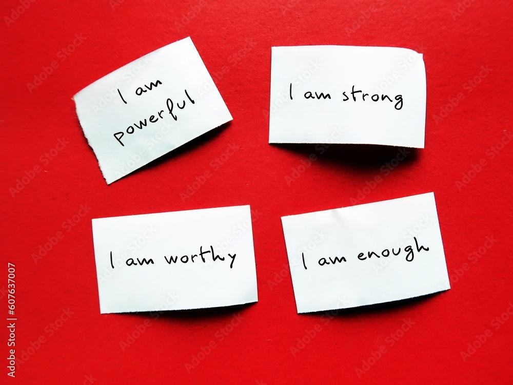 Four paper pieces on red background with handwritten text I AM STRONG, I AM WORTHY, I AM ENOUGH, I AM POWERFUL, positive self talk affirmations to boost self confidence Four paper pieces on red background with handwritten text I AM STRONG, I AM WORTHY, I AM ENOUGH, I AM POWERFUL, positive self talk affirmations to boost self confidence