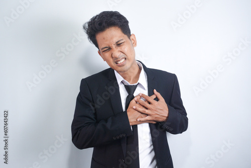 Young Asian man having heart ache, holding hand on chest. Heart attack or stroke, copy space