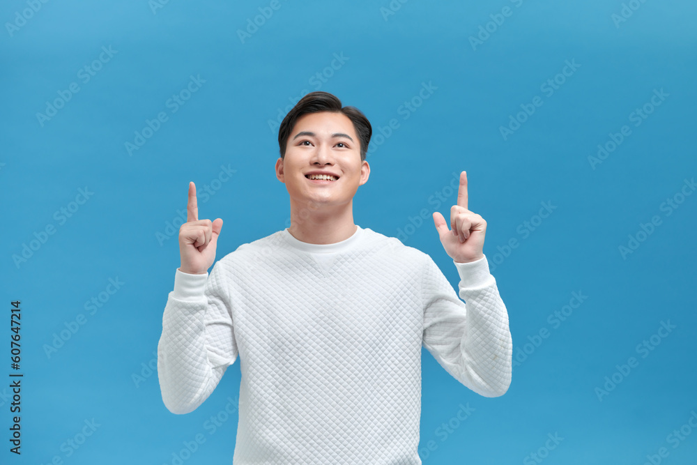 Happy handsome smiling young Asian man with hands poiting up to empty space above Happy handsome smiling young Asian man with hands poiting up to empty space above